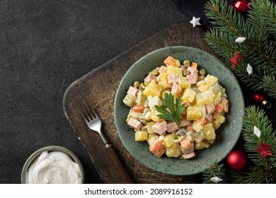 Traditional Russian Salad Olivier From Boiled Vegetables And Sausage With Mayo And Christmas Decorations On Black Table. Top View. Russian New Year Or Christmas Salad