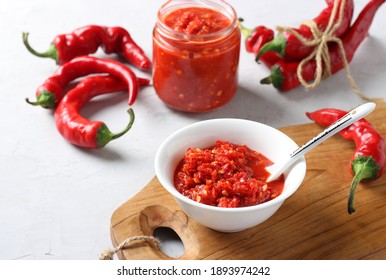 Traditional sauce adjika with hot chili pepper, paste harissa in bowl on wooden board.