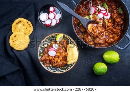 Traditional slow cooked Mexican pozole rojo with tortilla served as top view in a modern design cast-iron roasting dish on a rustic board