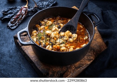 Traditional slow cooked Mexican pozole rojo soup with ground minced beef, hominy maiz and dry ancho paprika in cast-iron roasting dish on old rustic wooden board