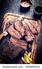 Traditional smoked barbecue wagyu beef brisket as piece and sliced offered as top view on an old cutting board with Louisiana sauce - vintage