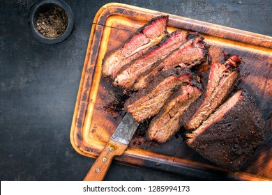 Traditional smoked barbecue wagyu beef brisket as piece and sliced offered as top view on an old cutting board with copy space left