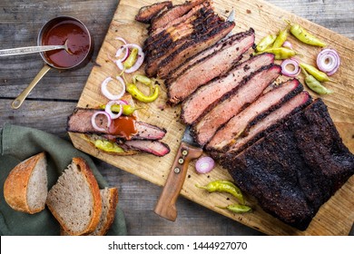 Traditional smoked barbecue wagyu beef brisket offered with farmhouse bread as top view on an old cutting board with Louisiana sauce, onion rings and peperoni 