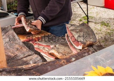 Traditional smoked speck sliced on site during a celebration in Val di Funes, Dolomites.