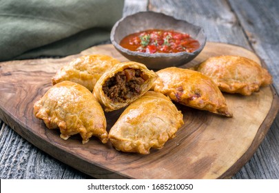Traditional South American empanada de carne offered with a chili dip as closeup on a rustic wooden board 