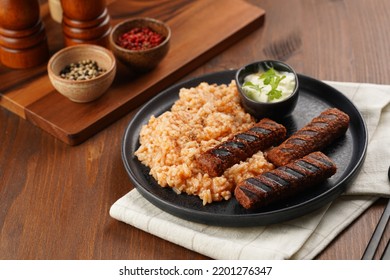 Traditional South European Skinless Sausages Cevapcici Made Of Ground Meat And Spices On Black Plate On Dark Wooden Board, Vegan Substitute Made Of Soy Protein, With Rice And Sour Cream