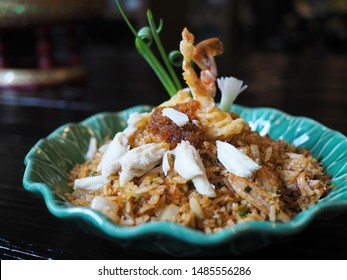 Traditional Southern Thai Hot And Spicy Stir Fried Rice, White Crab Meat, Crab Claw, Red Crab Legs, Chilis, Dried Shrimp Paste, Garlic, Herbs, Spring Onions, Egg On Green Leaf Plate On Wooden Table