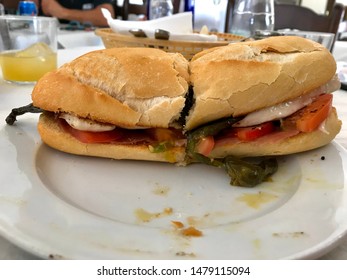 Traditional Spanish Chicken Sandwich With Fried Green Pepper, Tomato And Serrano Ham Cut In Half On A White Plate In Marbella, Spain