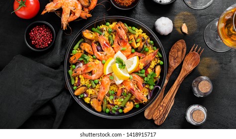 Traditional spanish seafood paella in the fry pan on a black wooden  table, top view.