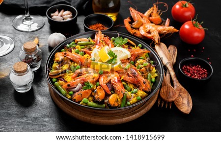 Traditional spanish seafood paella in the fry pan on a black wooden  table.