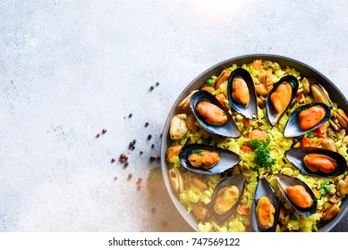 Traditional spanish seafood paella in pan rice, peas, shrimps, mussels, squid on light grey concrete background. Top view, copyspace