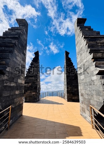 Traditional split gate at Seruni Point, a scenic viewpoint near Mount Bromo, Indonesia. The stone Balinese-style entrance contrasts with blue skies and clouds, creating a breathtaking travel and cultu