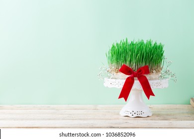 Traditional spring wheat grass semeni for Novruz celebration, Easter theme green background, red ribbon festive bow, wooden table spring equinox greeting card copy space Persian, Azerbaijan nowruz