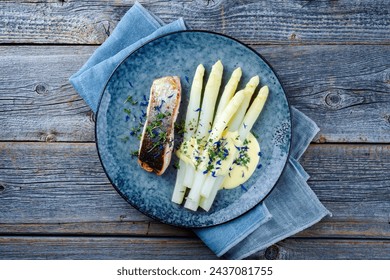 Traditional steamed white asparagus with salmon fillet and sauce hollandaise served as top view on a design plate with copy space
