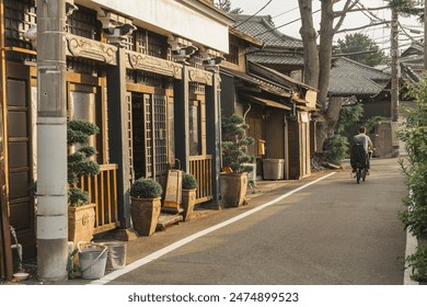 Traditional street level housing of Yanesen, Tokyo, Japan at sunset. A man with a bike is moving away from view along a pedestrian road. Scene of tranquillity. - Powered by Shutterstock