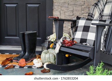 Traditional style front porch decorated for autumn with rain boots, heirloom gourds,  white pumpkins, mums and rocking chair with buffalo plaid pillow and throw blanket giving an inviting atmosphere.
