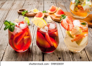Traditional summer drink sangria - red, pink and white. With champagne, pink and red wine, strawberries, oranges, lemon, green apple and grapefruit. On a wooden rustic table, copy space