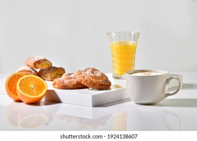 Traditional sweet pastries surrounded by a coffee cup, orange juice and an orange cut in half on a table. Traditional breakfast concept.