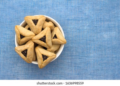 Traditional sweets for Jewish holiday of Purim. Hamantashen cookies or Aman ears, triangular cookies with poppy seeds on blue background, top view, free space
