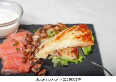 A Traditional Swiss Dish Is Strung On A Fork - Part Of A Potato Pancake. In The Background, You Can See The Food On The Board For Serving Dishes.