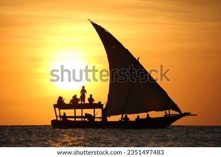 A traditional Tanzanian dhow silhouetted against the setting sun.
