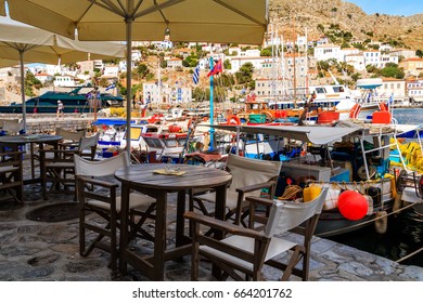 Traditional Tavern Cafe With Wooden Tables And Chairs Outside Near The Fishing Boats In Port Of Hydra Island In Greece