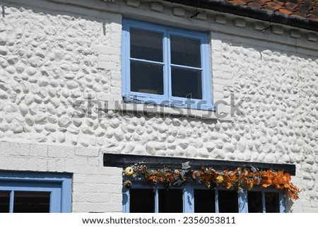 Traditional terraced cottage made of whitewashed flint stone walling with colourful red clay tiled roof and blue windows in Holt, Norfolk, England