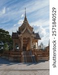 Traditional Thai temple pavilion in Phuket, Thailand, featuring intricate carvings, tiered roofs, a golden spire, and a surrounding paved courtyard.