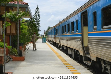Traditional thai train is pulling into rural station with person standing and waving green flag to signal safety, passenger train approaching platform. authentic atmosphere of northern thailand rail travel