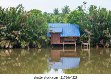 Traditional Thai wooden house with Nipa palms growing by river with reflection on still water in Amphawa District, Samut Songkhram, Thailand.