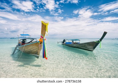 Traditional Thai wooden longtail boats with decorative sash ribbons moored in crystal waters on the shore of Bamboo Island near Krabi