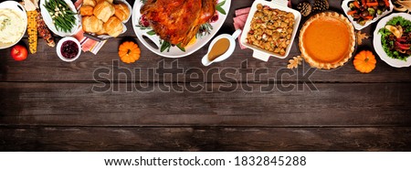 Traditional Thanksgiving turkey dinner. Above view top border on a dark wood banner background with copy space. Turkey, mashed potatoes, dressing, pumpkin pie and sides.