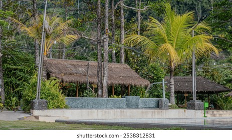 traditional thatched-roof hut surrounded by palm trees and lush greenery. A swimming pool is in the foreground. - Powered by Shutterstock