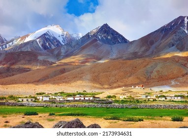 Traditional Tibet village, temple and green field at the background of colorful high mountain range with snow and cloudy blue sky. Beautiful view in Merak, Ladakh, Jammu  Kashmir, India, Central Asia