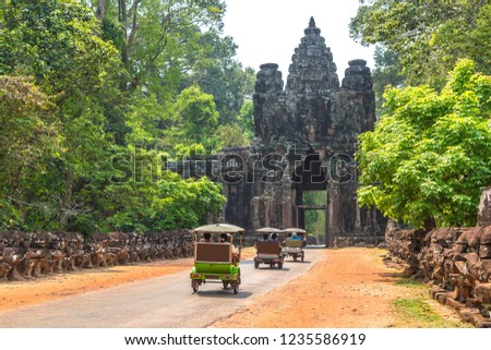 Traditional Tuk Tuk on a road and South gate to Angkor Thom, near Siem Reap, Cambodia in a summer day