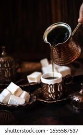 Traditional turkish coffee and turkish delight in traditional oriental copper serving set. Coffee pouring from cezve into a cup. Dark vintage background