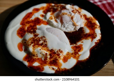 Traditional Turkish cuisine dish prepared with poached eggs, yogurt and butter with red pepper flakes on a black plate. Its traditional name is Çılbır. - Shutterstock ID 2108964101