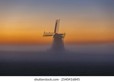 Traditional typical Frisian Dutch wind mill, windmill and wind turbine at orange dawn sunrise in fog mist and bird - Powered by Shutterstock