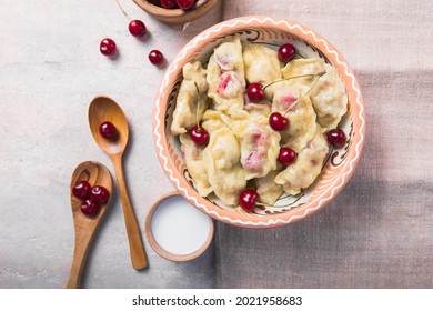 Concepto de cocina tradicional ucraniana. Varenyky con cerezas. Una porción de bolas listas para comer en un plato de arcilla marrón con crema agria, salpicada de azúcar por encima. Comida casera.