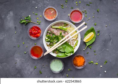 Traditional Vietnamese Noodle Soup Pho In Bowl, Garnished With Basil, Mint, Lime, On Concrete Background
