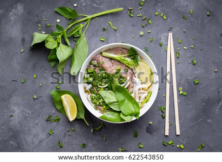 Traditional vietnamese noodle soup pho in bowl, garnished with basil, mint, lime, on concrete background
