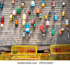 Traditional vintage lobster buoys hanging on the wall of a building with yellow lobster pots on the ground in Portland Maine USA.