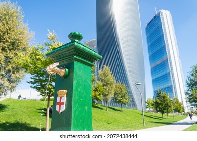 Traditional water fountain in the business district of Milan, named "Citylife". Tall skyscrapers and blue sky in the blurred background. Selective focus.