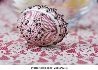 Traditional wax painted Easter egg  against a red and white lacy background