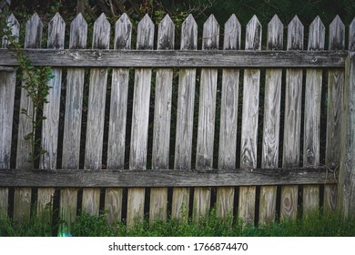 Traditional Weathered  Wooden Picket Fence Showing Wear And Aged Texture With Overgrown Weeds At Bottom