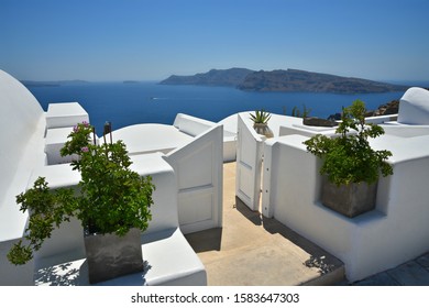 Traditional Whitewashed Adobe House With Arched Rooftop, Wooden Entrance Door And Stone Steps Overlooking The Aegean Sea In Santorini Island, Cyclades Greece. 