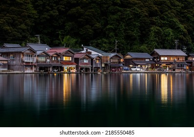 Traditional wooden boathouses reflect of calm water as night falls on Ine, Kyoto