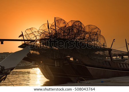 A traditional wooden dhow boat at sunset loaded with empty lobster pots ready to go out to sea for a fishing trip with a golden orange sunset background