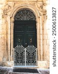 Traditional wooden green doorway with ornate white steel gate and limestone scultpures.