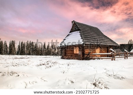Traditional Wooden House in Winter Woods at Sunset.